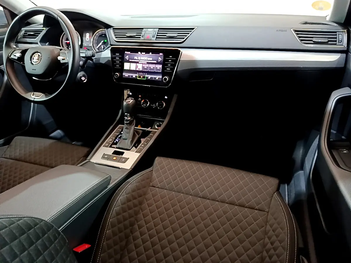 Intérieur de la Skoda Superb 2020 vu côté conducteur, sièges noirs matelassés et écran tactile central allumé.