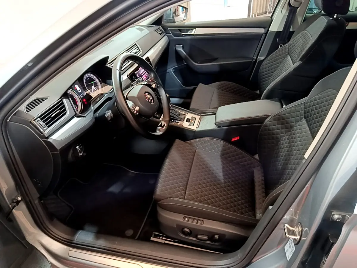 Intérieur côté conducteur de la Skoda Superb gris clair 2020, sièges noirs matelassés et tableau de bord moderne.