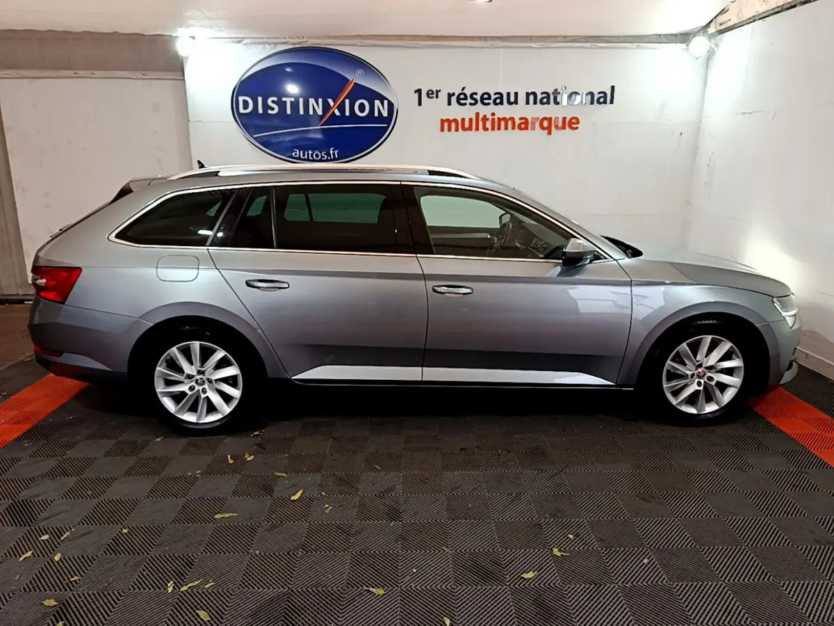 Profil côté droit d'une Skoda Superb gris clair 2020 en version break, stationnée en intérieur sur sol damier.