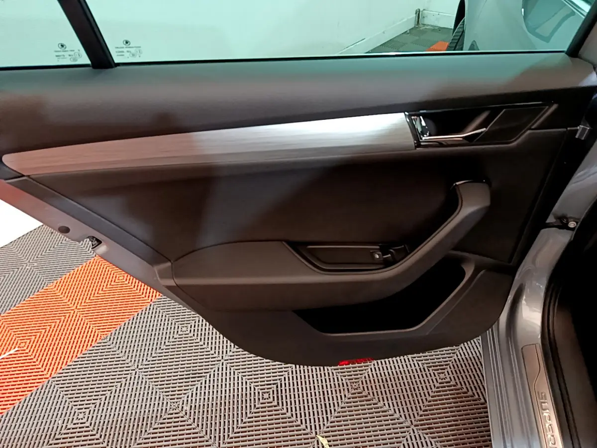 Vue intérieure de la porte côté gauche d'une Skoda Superb gris clair, avec garniture noire et insert décoratif argenté.