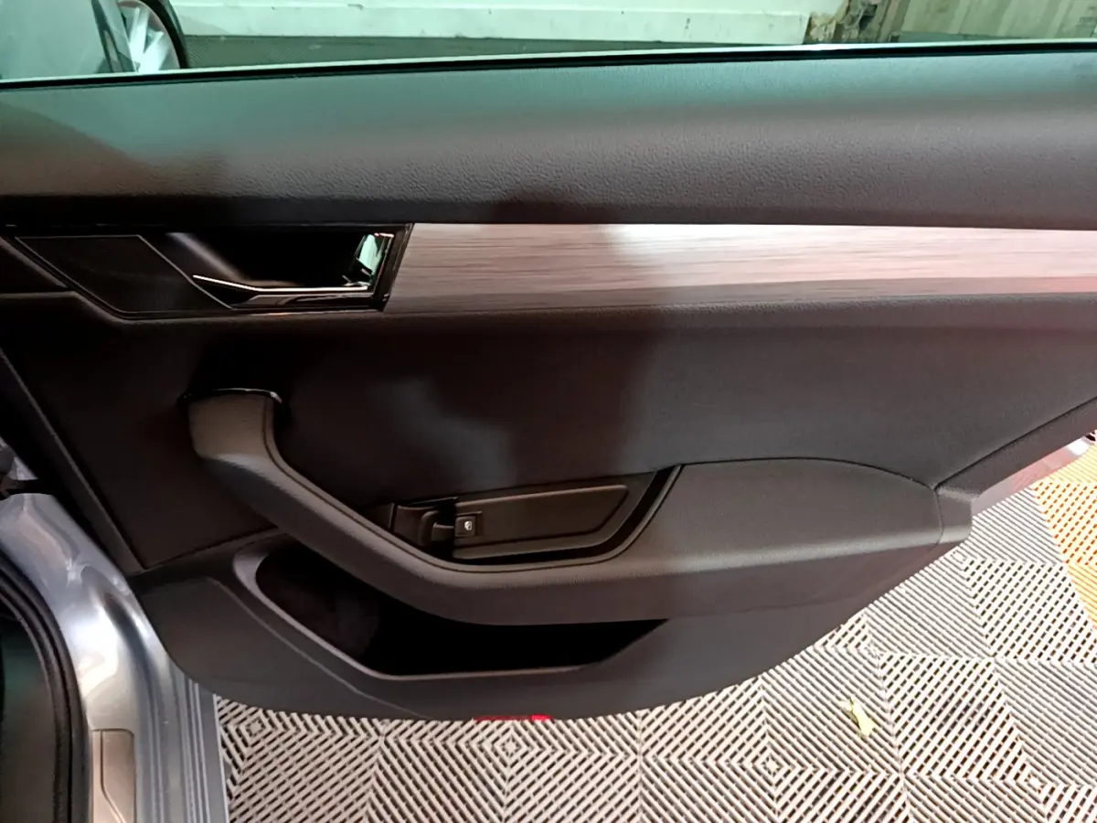 Intérieur côté gauche de la porte d'une Skoda Superb gris clair, avec poignée noire et insert décoratif bois clair.