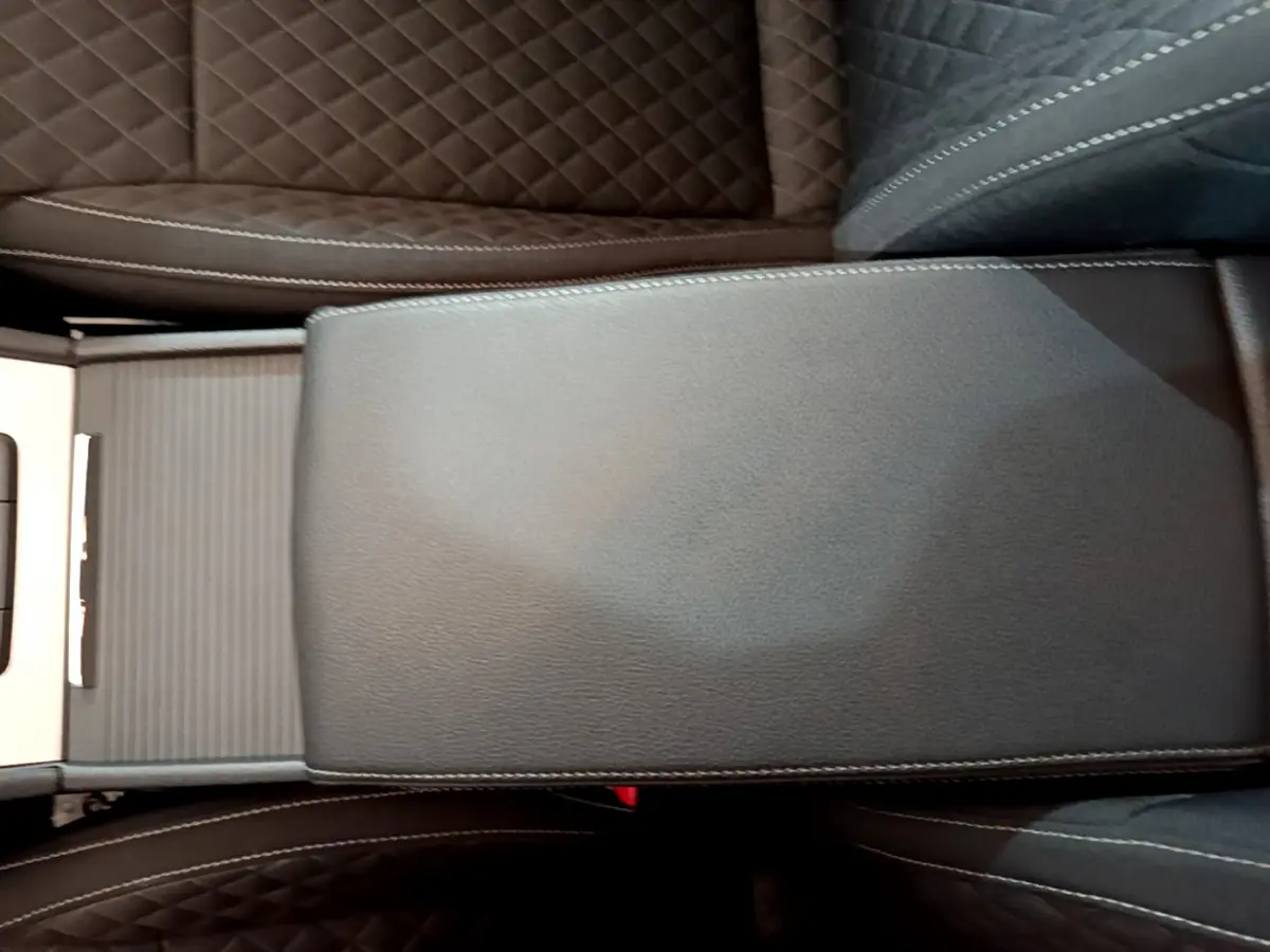 Gros plan sur l'accoudoir central en cuir noir avec surpiqûres blanches, entre les sièges marron matelassés de la Skoda Superb.