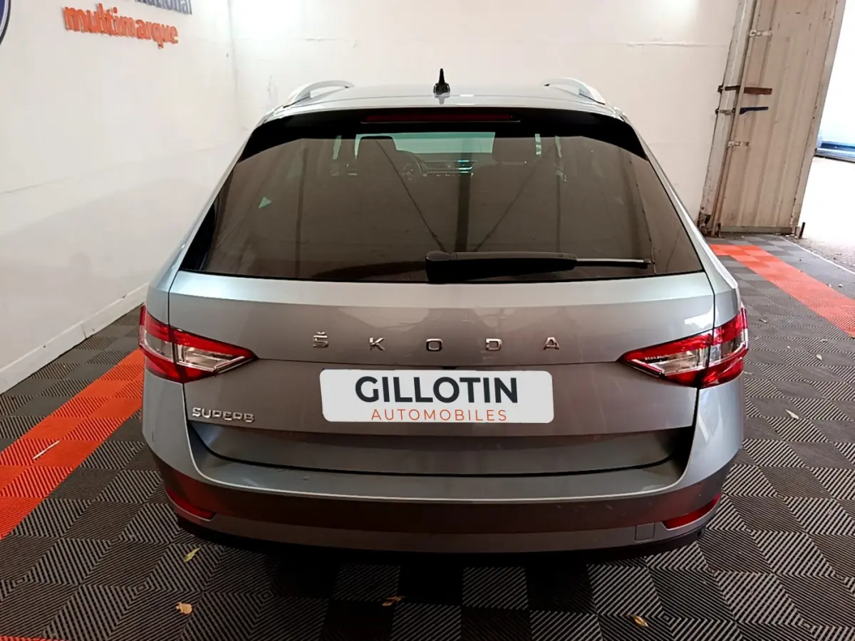 Vue arrière d'une Skoda Superb gris clair stationnée en intérieur avec feux arrière LED et logo visible.