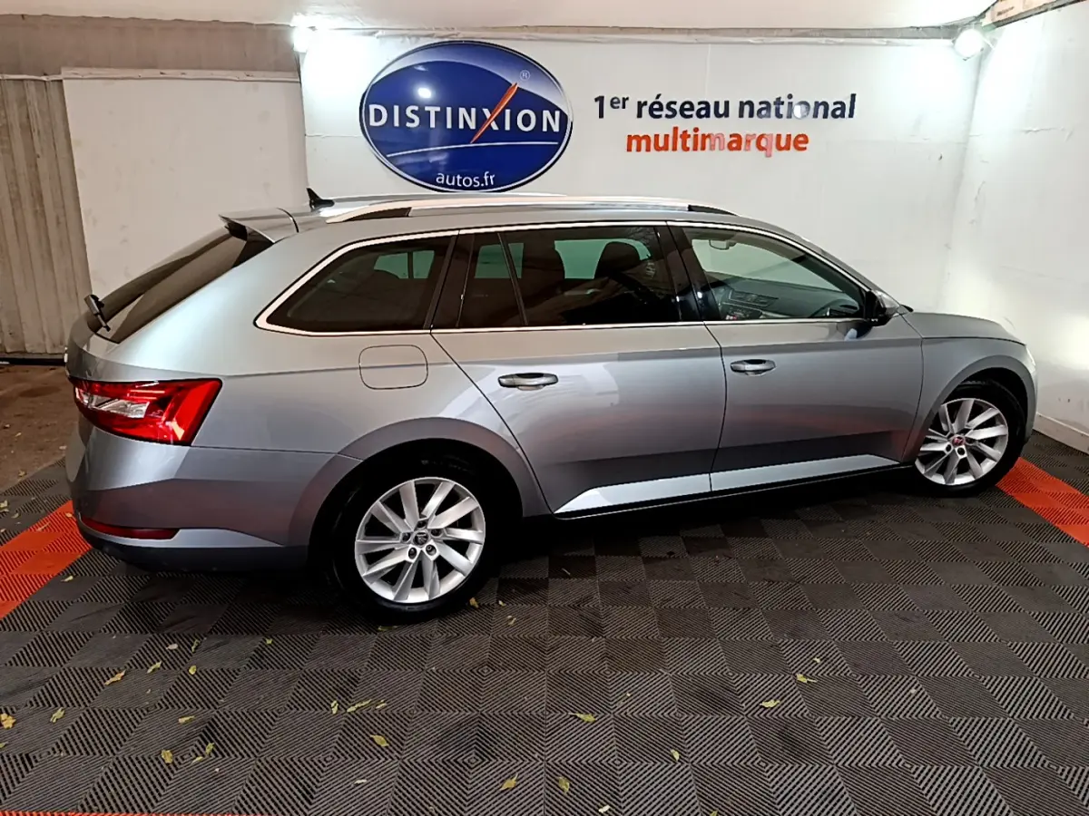 SKODA SUPERB break gris clair vu de profil côté gauche dans un showroom avec logo Distinxion en arrière-plan.