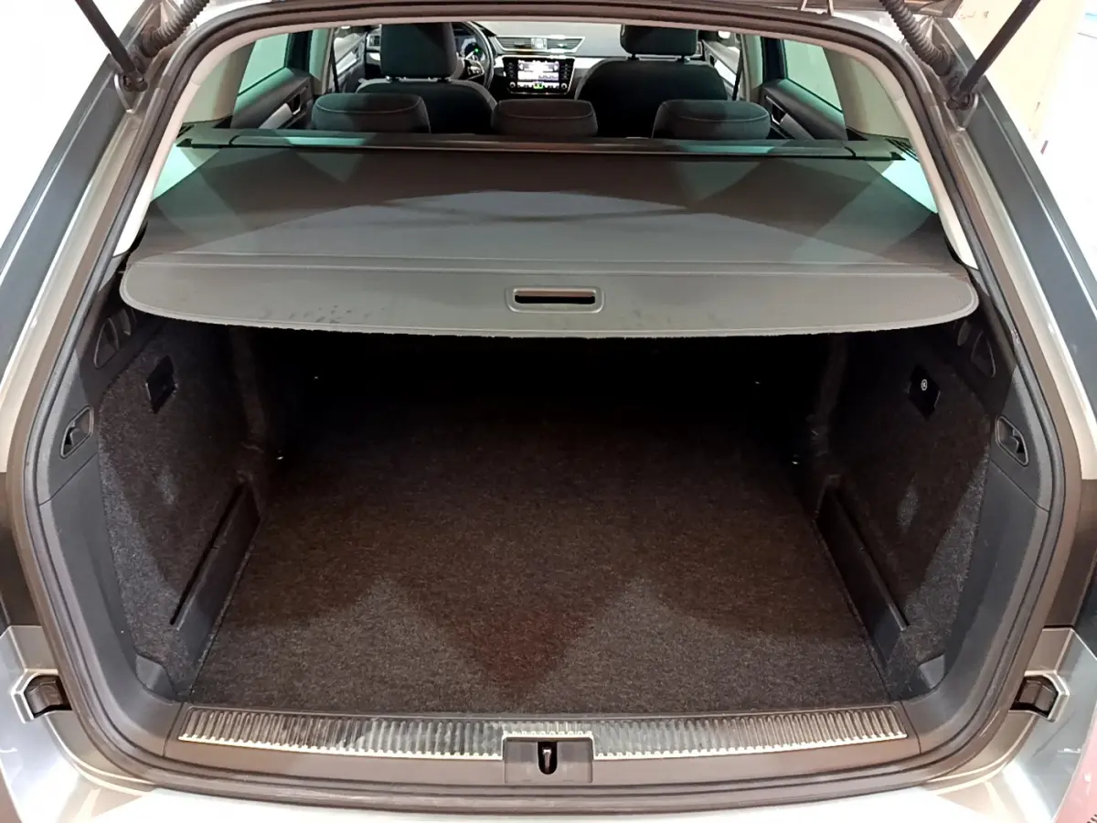 Coffre ouvert d’une SKODA SUPERB gris clair, vue arrière montrant l’espace de chargement et la tablette cache-bagages.
