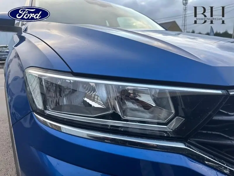 Gros plan sur le phare avant gauche du Volkswagen T-Roc bleu Ravenna métallisé, mettant en valeur les détails du bloc optique.