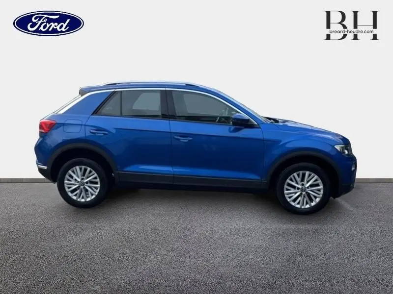Profil droit d'un Volkswagen T-Roc 2021 bleu Ravenna métallisé avec jantes alliage et barres de toit noires.