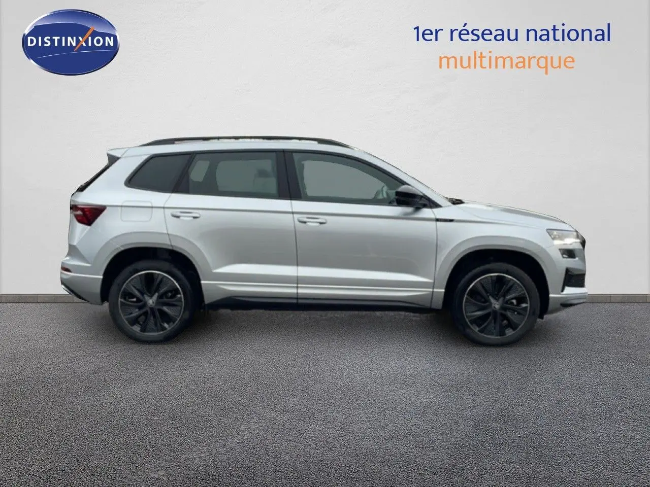 Profil droit d’un Skoda Karoq 1.5 TSI 150ch Sportline gris argent métallisé avec jantes noires sur fond neutre.