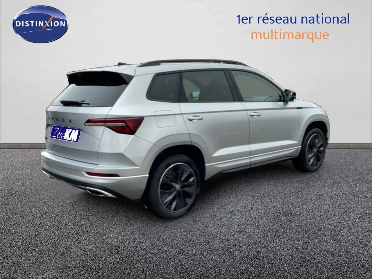Vue 3/4 arrière droite d’un Skoda Karoq gris argent métallisé avec jantes noires et toit ouvrant panoramique.