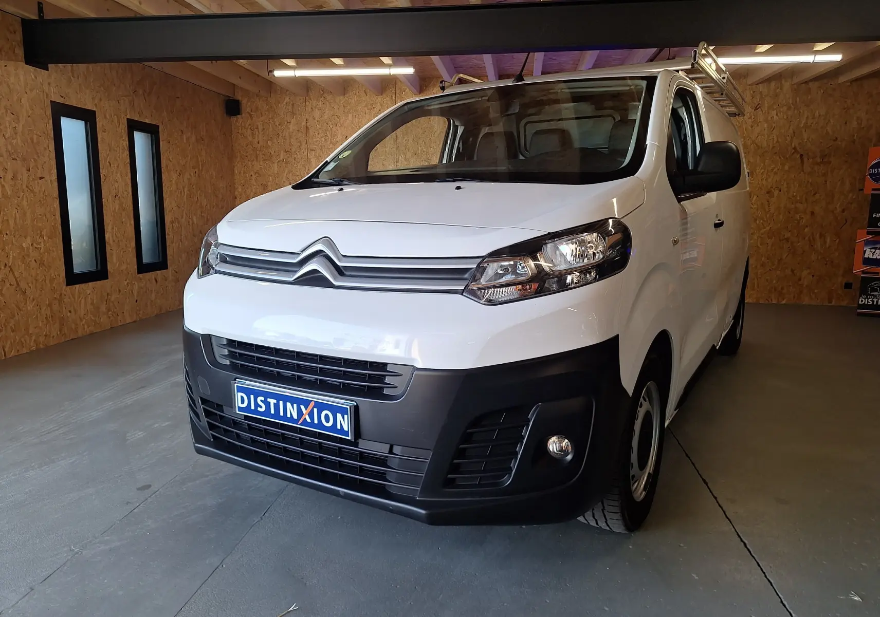 Citroën Jumpy blanc en 3/4 avant droit dans un garage avec calandre noire et plaque Distinxion visible.