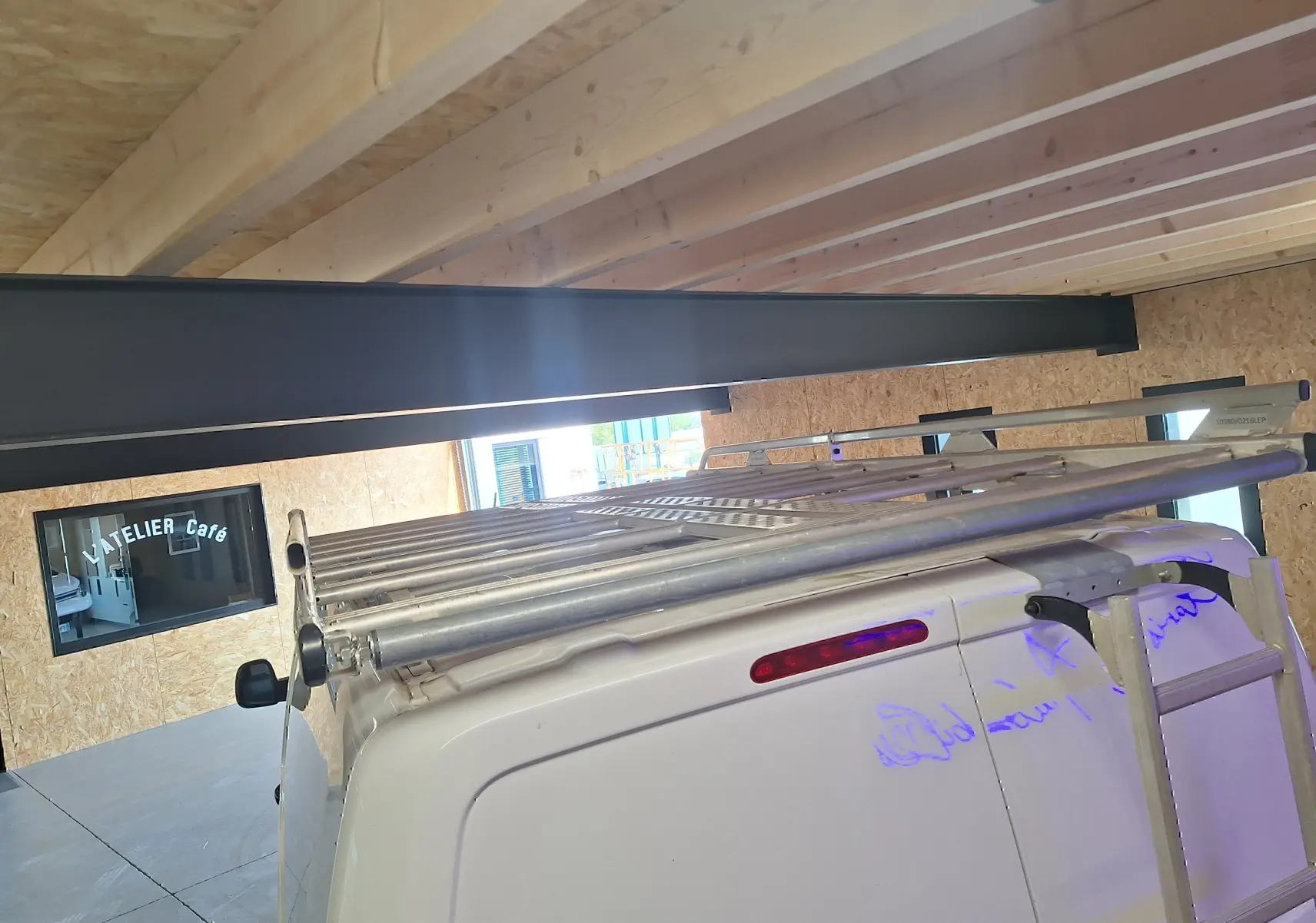 Vue arrière en plongée d'un Citroën Jumpy blanc avec galerie et échelle métallique sur le toit dans un garage.