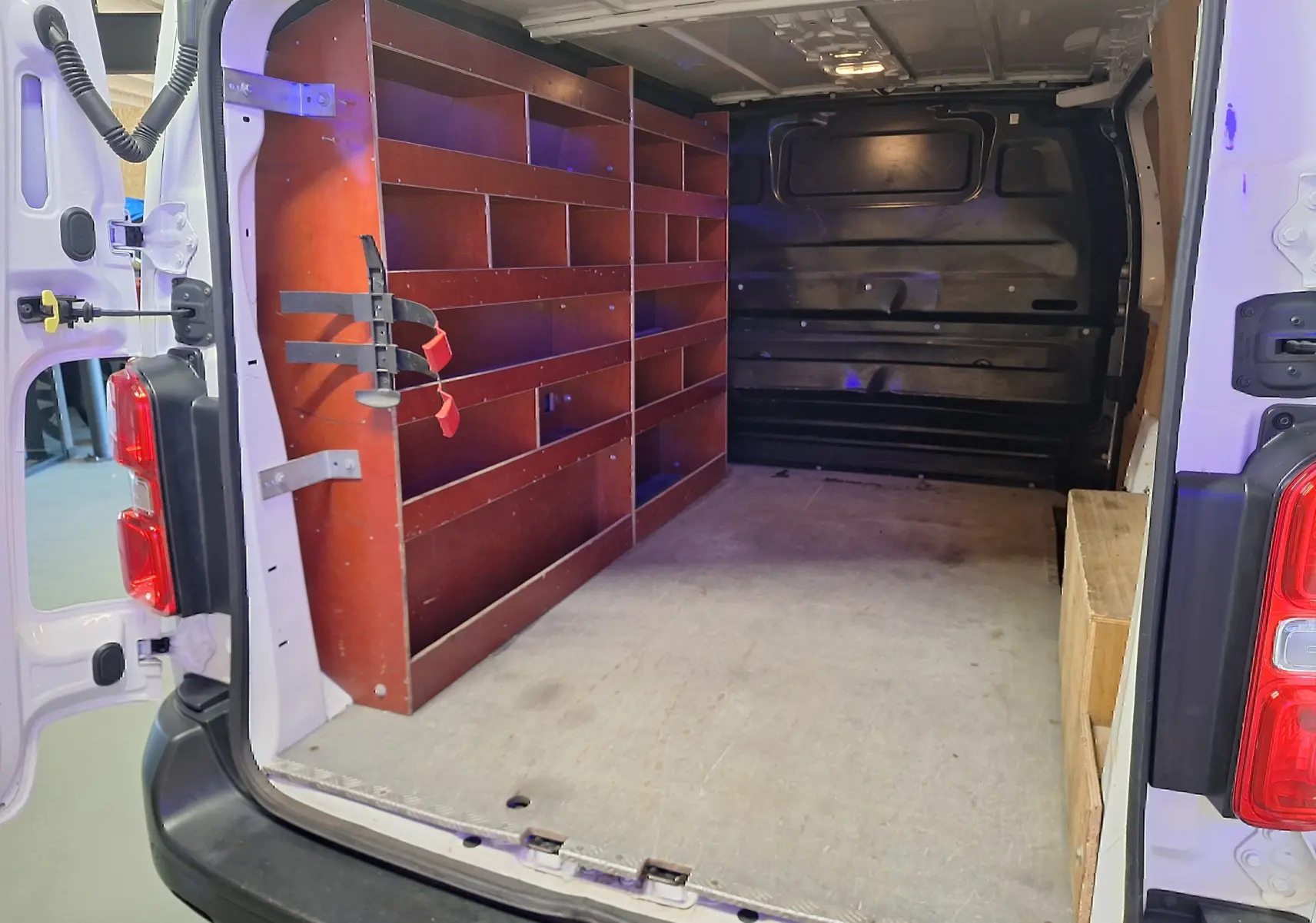 Vue intérieure arrière du Citroën Jumpy blanc 2020 montrant l'aménagement avec étagères en bois sur le côté gauche.