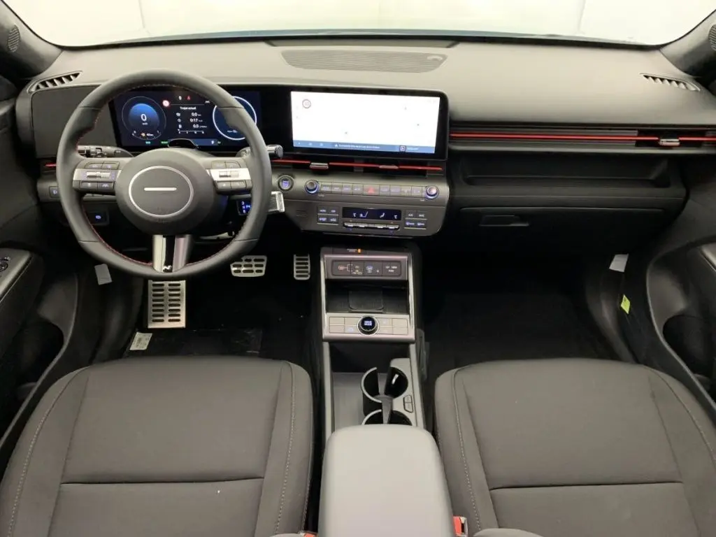 Vue intérieure frontale du tableau de bord du Hyundai Kona Hybrid 2025, avec écran tactile large et volant multifonction noir.