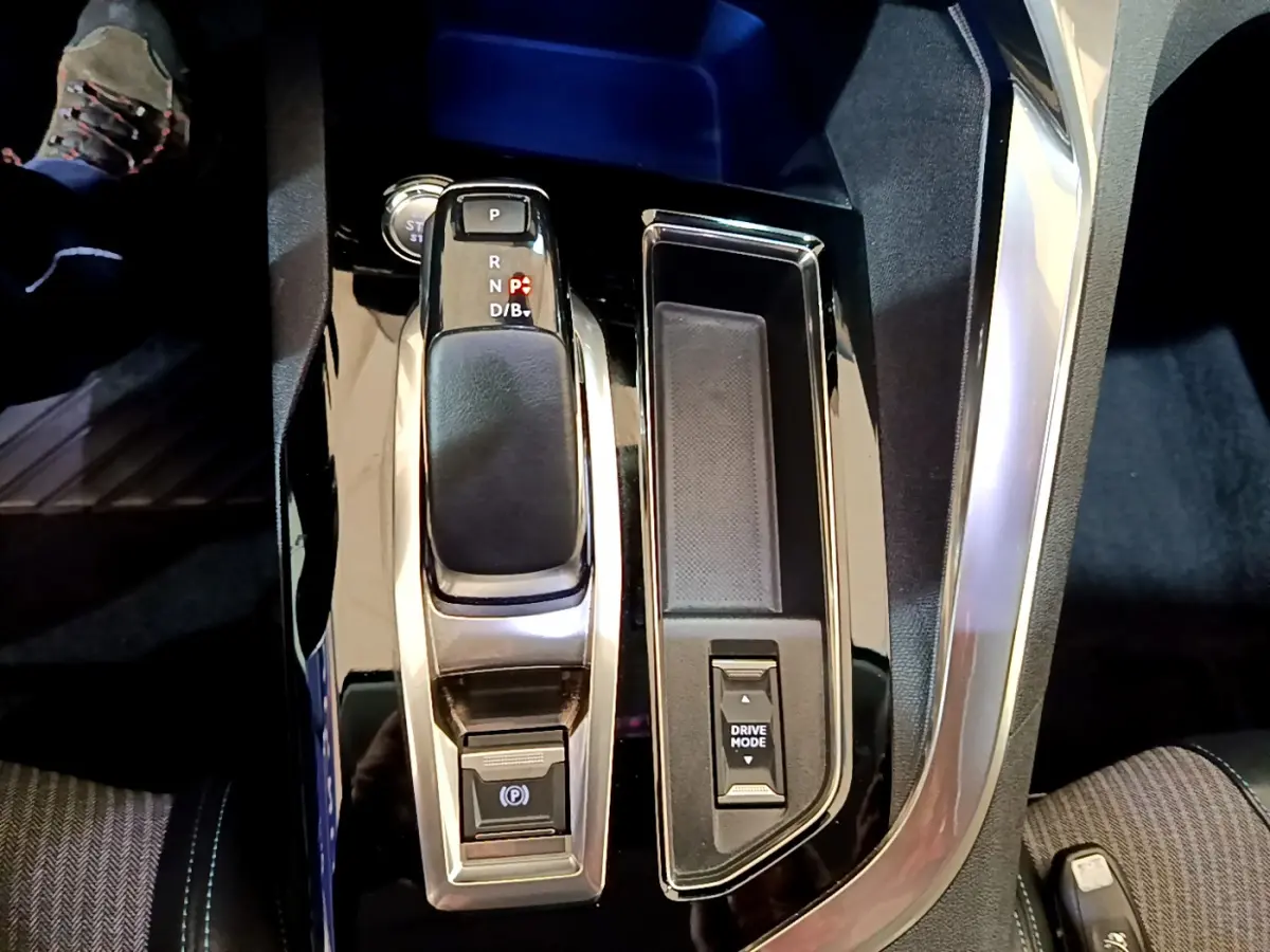 Vue rapprochée de la console centrale noire brillante du Peugeot 3008 hybride avec levier de vitesses et bouton Drive Mode.