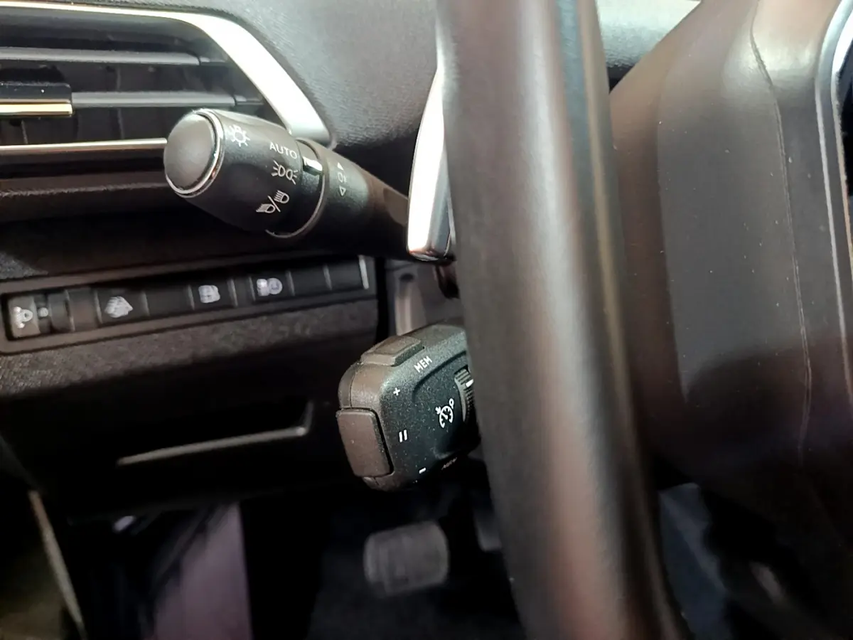 Gros plan sur les commandes au volant et la manette d'éclairage du Peugeot 3008 hybride bleu, intérieur noir.