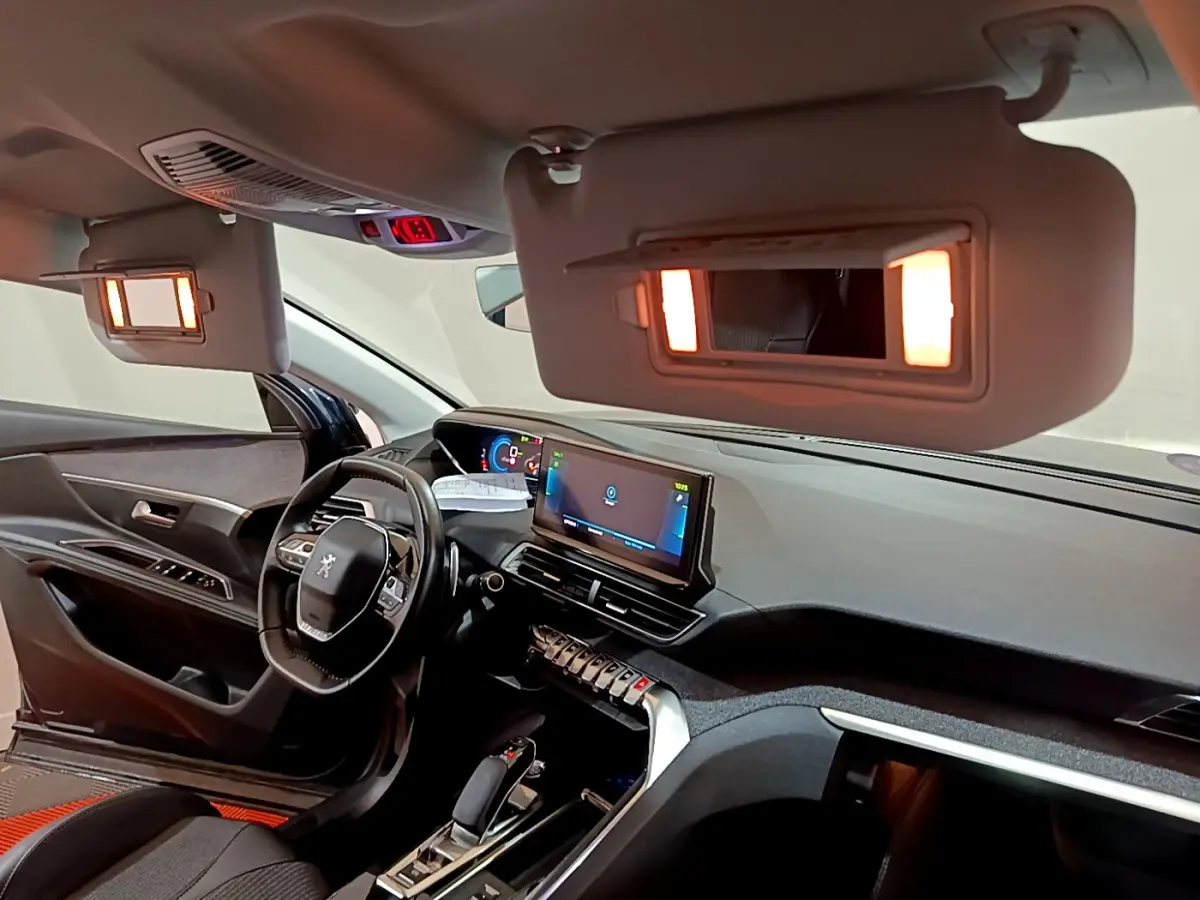 Intérieur du Peugeot 3008 bleu 2021, vue côté conducteur, tableau de bord numérique et miroirs de courtoisie éclairés.