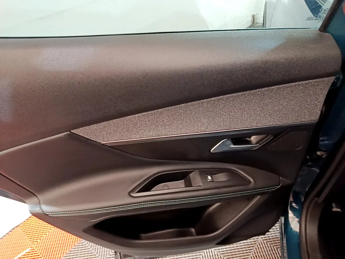 Gros plan sur la porte côté gauche intérieure du Peugeot 3008 bleu, avec garniture noire et bouton de vitre électrique.