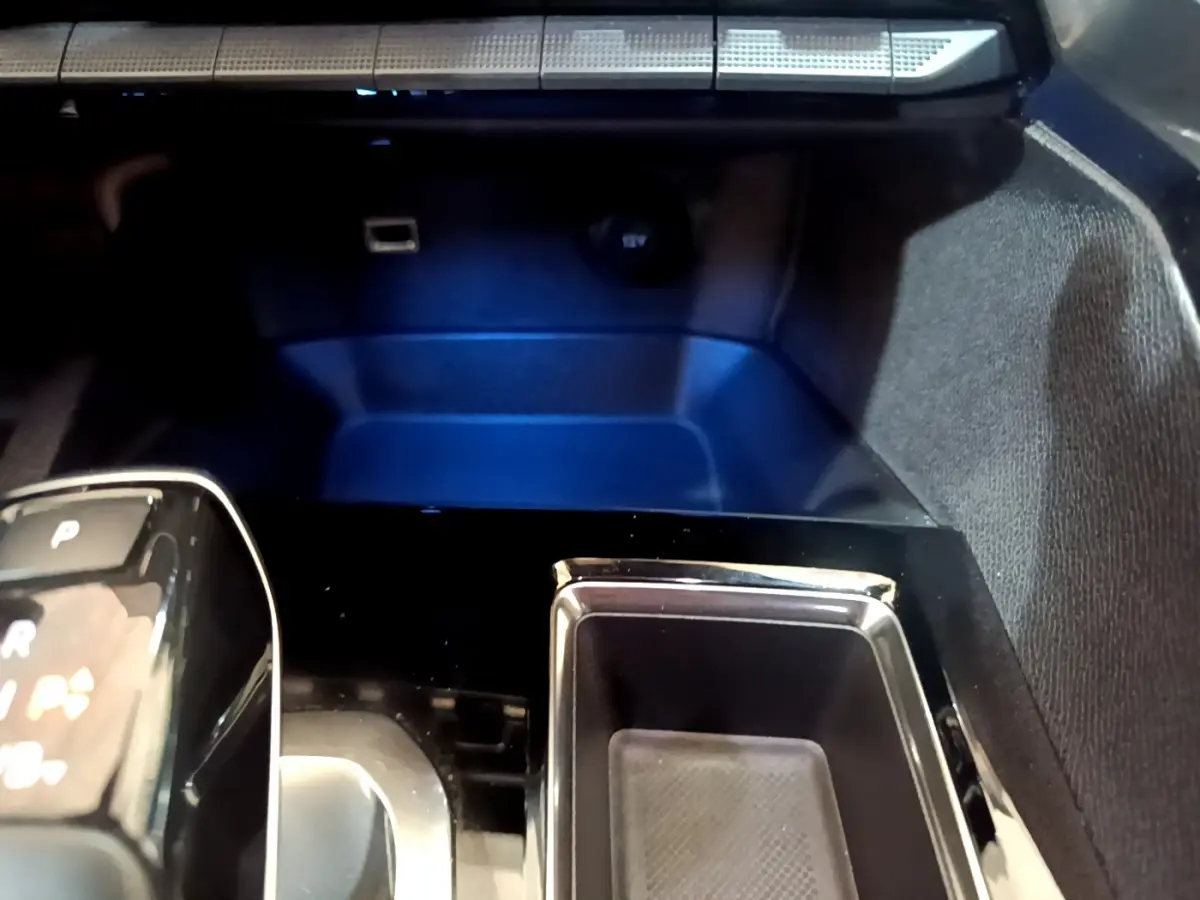 Gros plan sur la console centrale noire brillante du Peugeot 3008 bleu, avec levier de vitesses automatique et prise 12V visible.