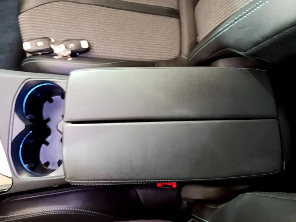 Gros plan sur l'accoudoir central noir et porte-gobelets éclairés en bleu du Peugeot 3008 hybride rechargeable bleu 2021.