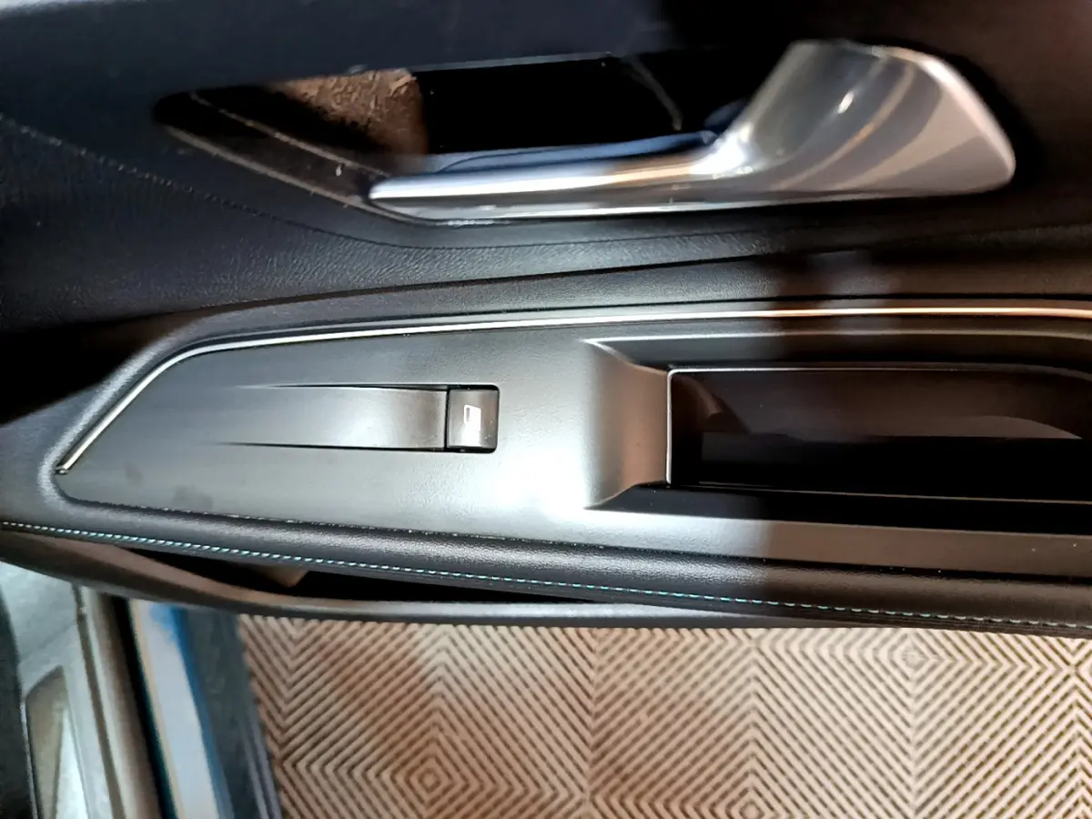 Gros plan sur la poignée intérieure côté gauche de la porte d’un Peugeot 3008 bleu avec bouton de lève-vitre intégré.