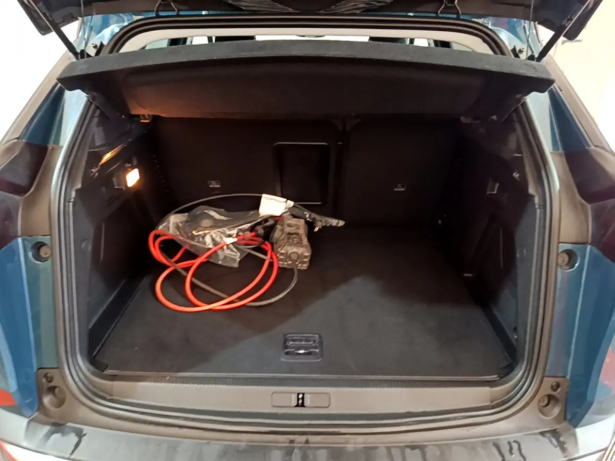 Coffre ouvert d’un Peugeot 3008 bleu, vue arrière montrant un câble de recharge hybride et un intérieur spacieux noir.