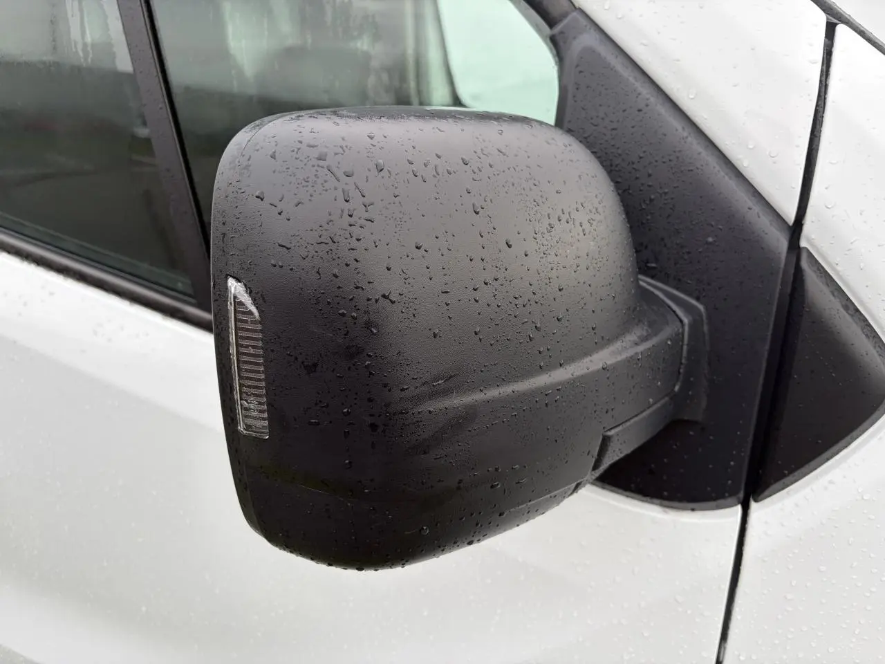 Gros plan sur le rétroviseur noir côté droit du Renault Trafic Fourgon blanc glacier avec gouttes de pluie visibles.