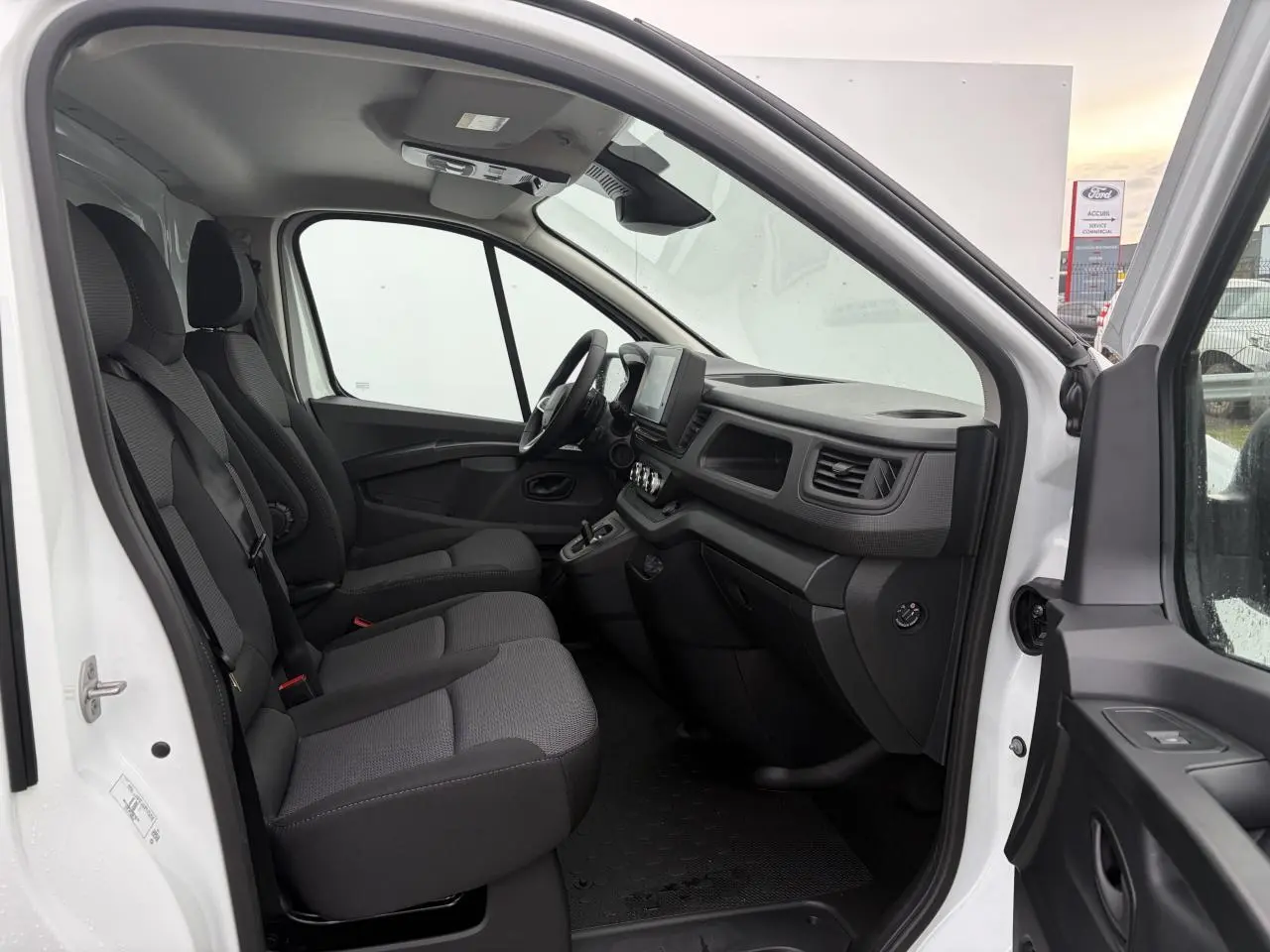 Vue intérieure côté conducteur du Renault Trafic Fourgon blanc Glacier, montrant les sièges tissu et le tableau de bord avec écran tactile.