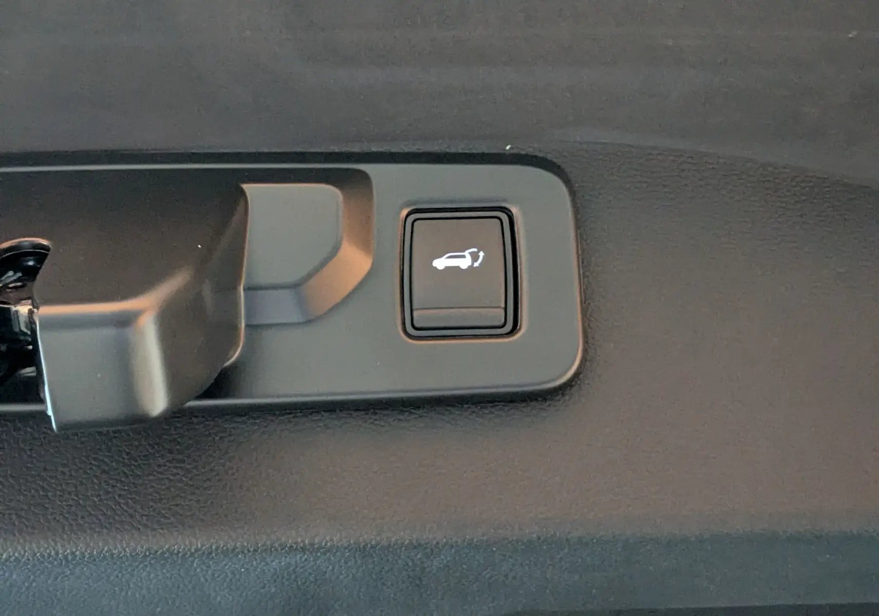 Gros plan sur le bouton d'ouverture électrique du hayon, intérieur noir du Renault Austral gris schiste.