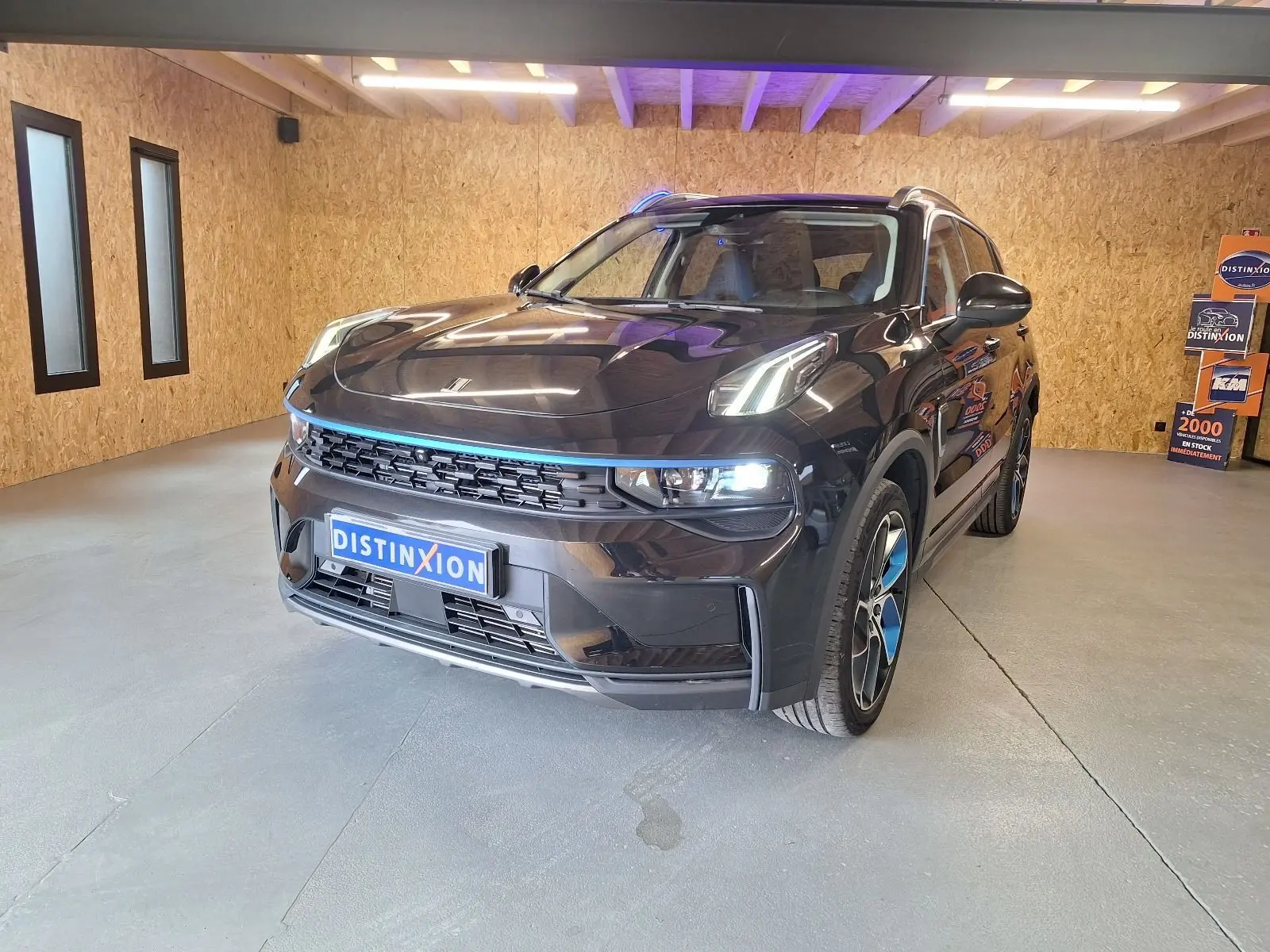 Vue 3/4 avant du SUV LYNK & CO 01 noir avec détails bleus sur la calandre et jantes dans un garage éclairé.