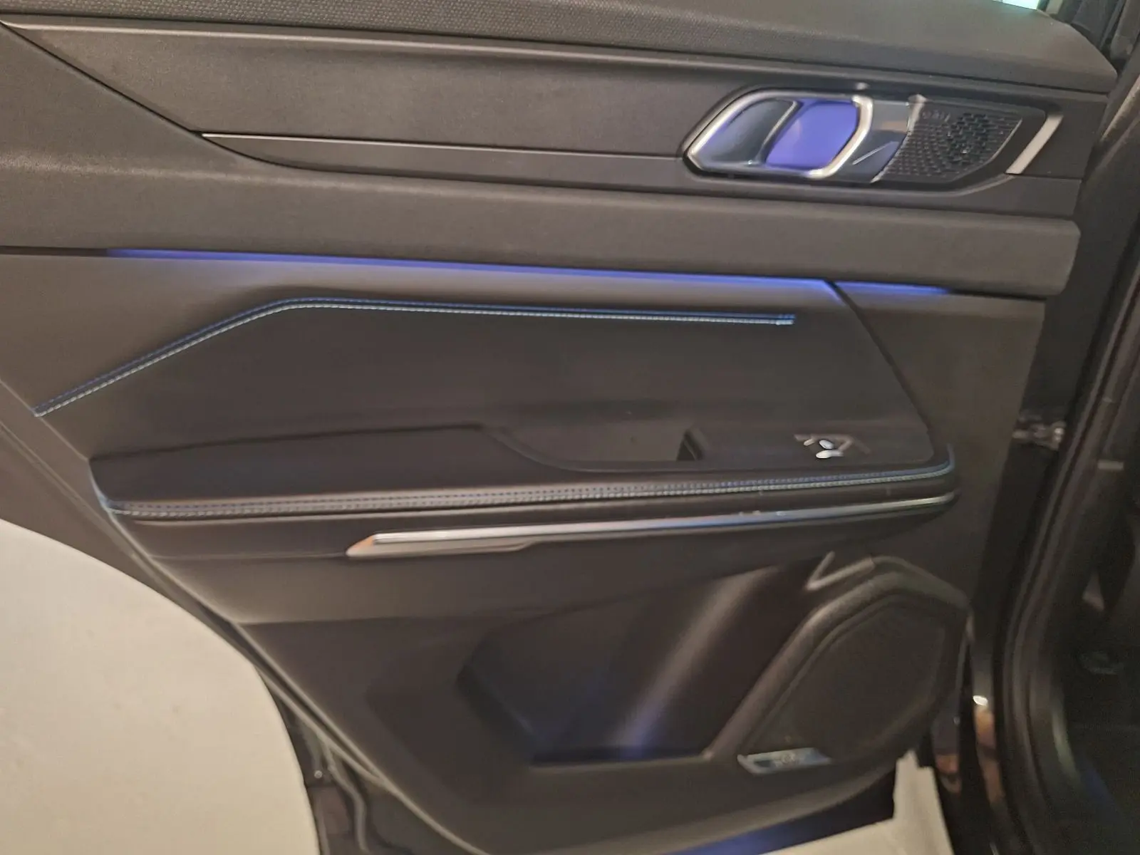 Intérieur de la porte côté gauche du Lynk & Co 01 noir 2023, avec éclairage bleu et surpiqûres contrastantes.