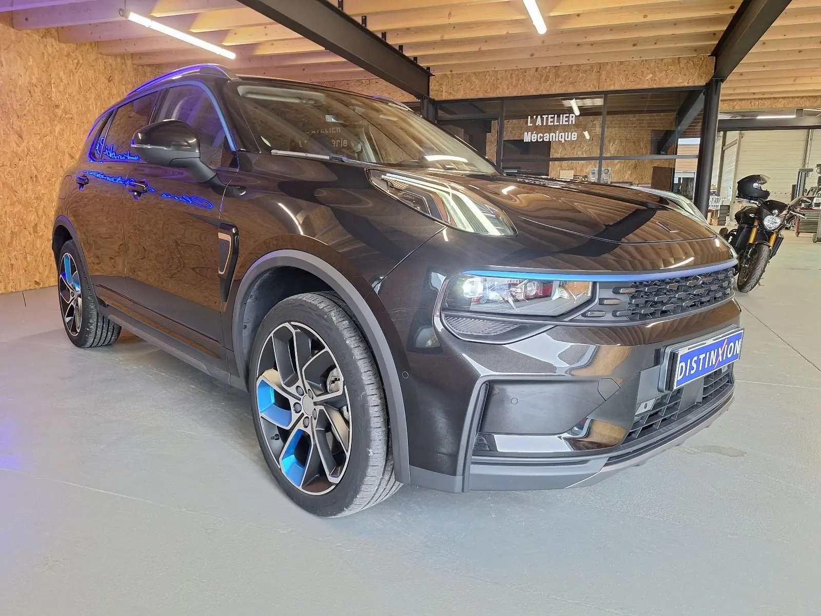 Lynk & Co 01 noir en 3/4 avant droit, avec jantes bicolores bleu et noir, dans un atelier mécanique intérieur.