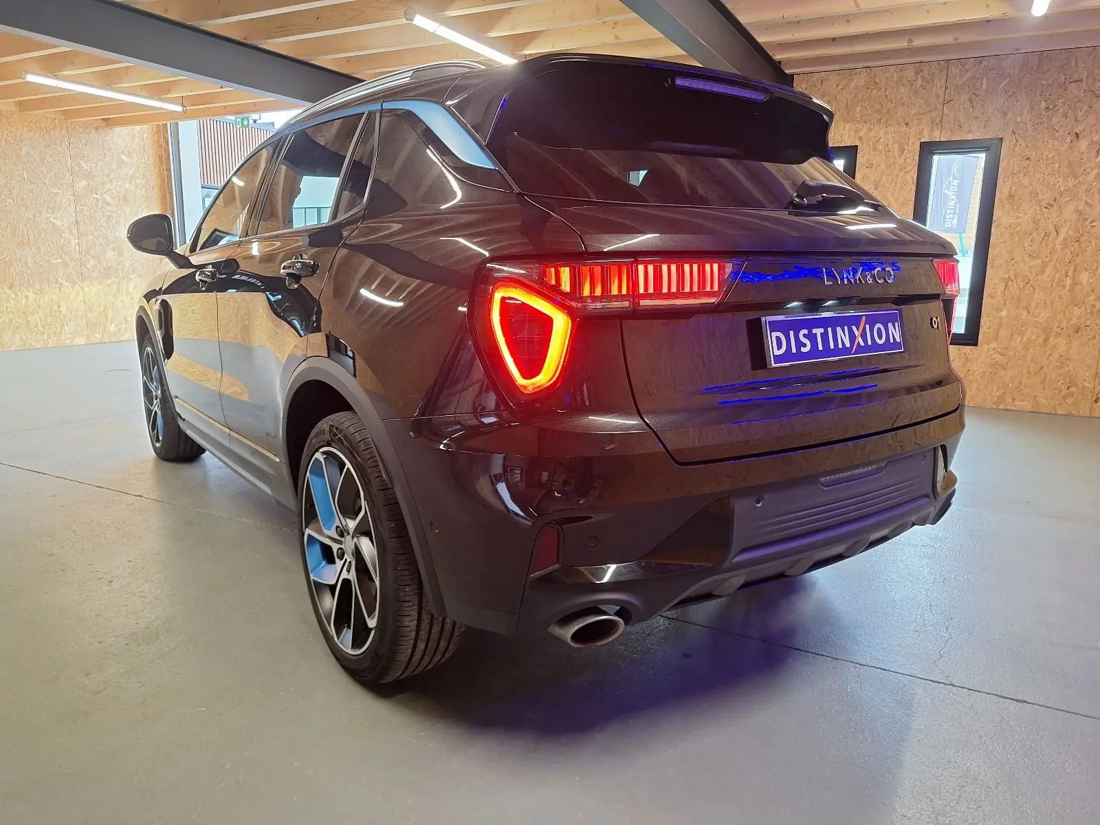 Vue 3/4 arrière droite d'un SUV LYNK & CO 01 noir avec feux arrière allumés dans un intérieur clair.