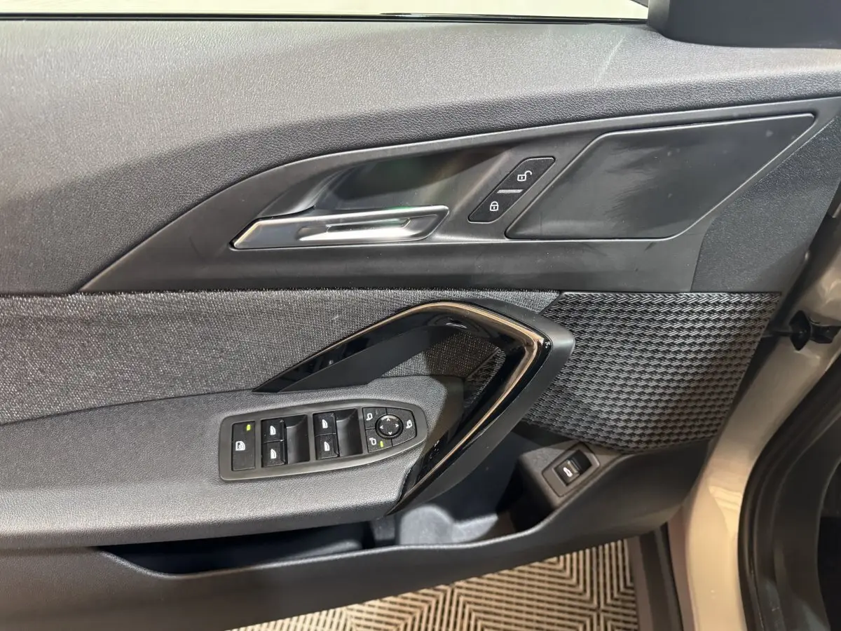 Vue rapprochée de la porte avant gauche gris foncé de la BMW X1 avec commandes électriques et insert décoratif texturé.