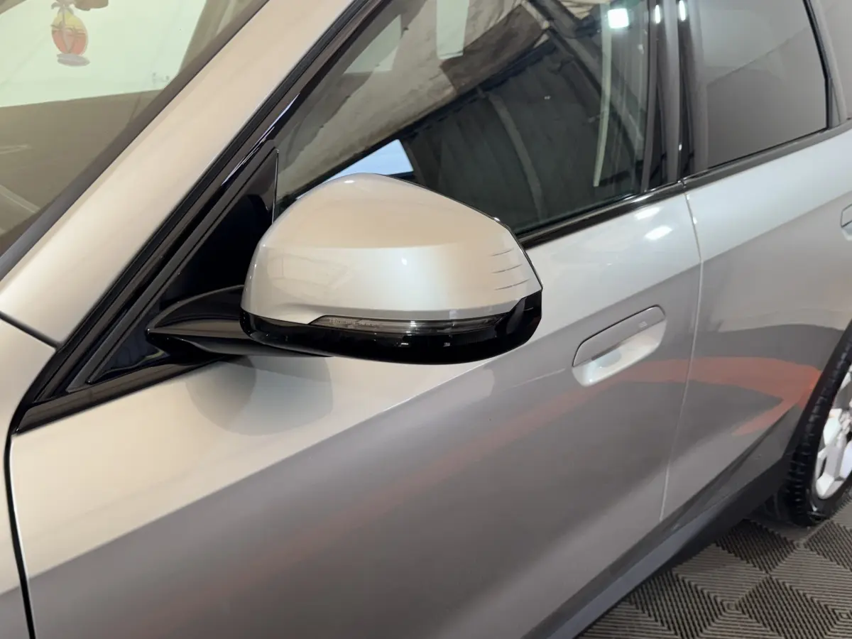 Gros plan sur le rétroviseur côté conducteur gris clair du BMW X1 sDrive20i 2024, avec porte et poignée visibles.