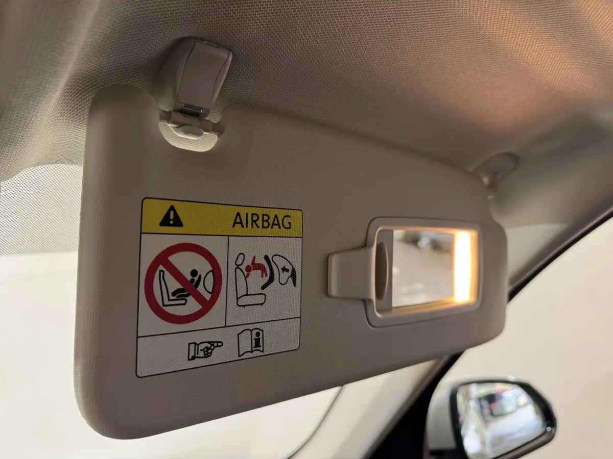 Détail du pare-soleil côté conducteur beige avec miroir éclairé et avertissement airbag, rétroviseur extérieur visible.