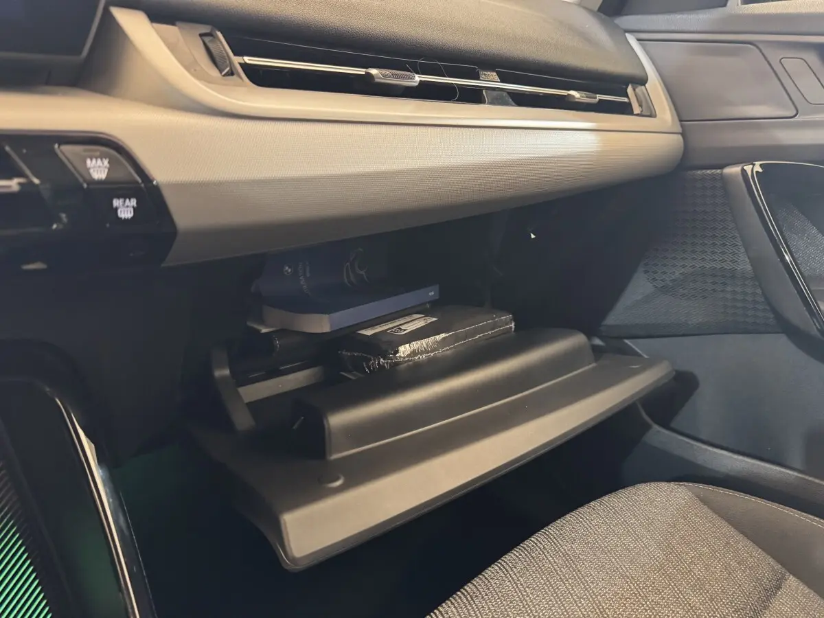 Vue intérieure côté passager du BMW X1 2024 gris foncé, boîte à gants ouverte avec objets rangés visibles.