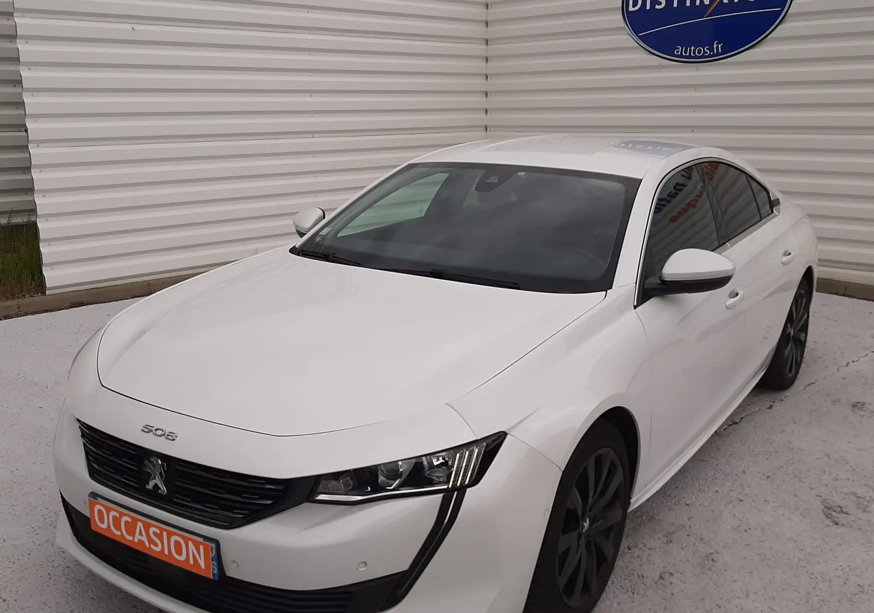 Peugeot 508 blanche vue en 3/4 avant droit, avec calandre noire et jantes foncées, stationnée devant un mur blanc.