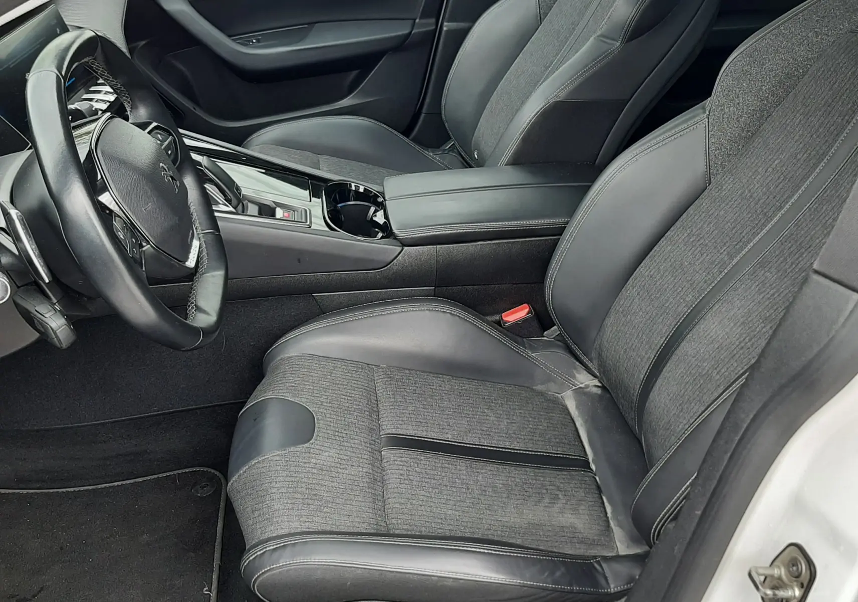 Vue intérieure côté conducteur de la Peugeot 508 blanche, montrant les sièges en tissu et cuir gris et la console centrale moderne.