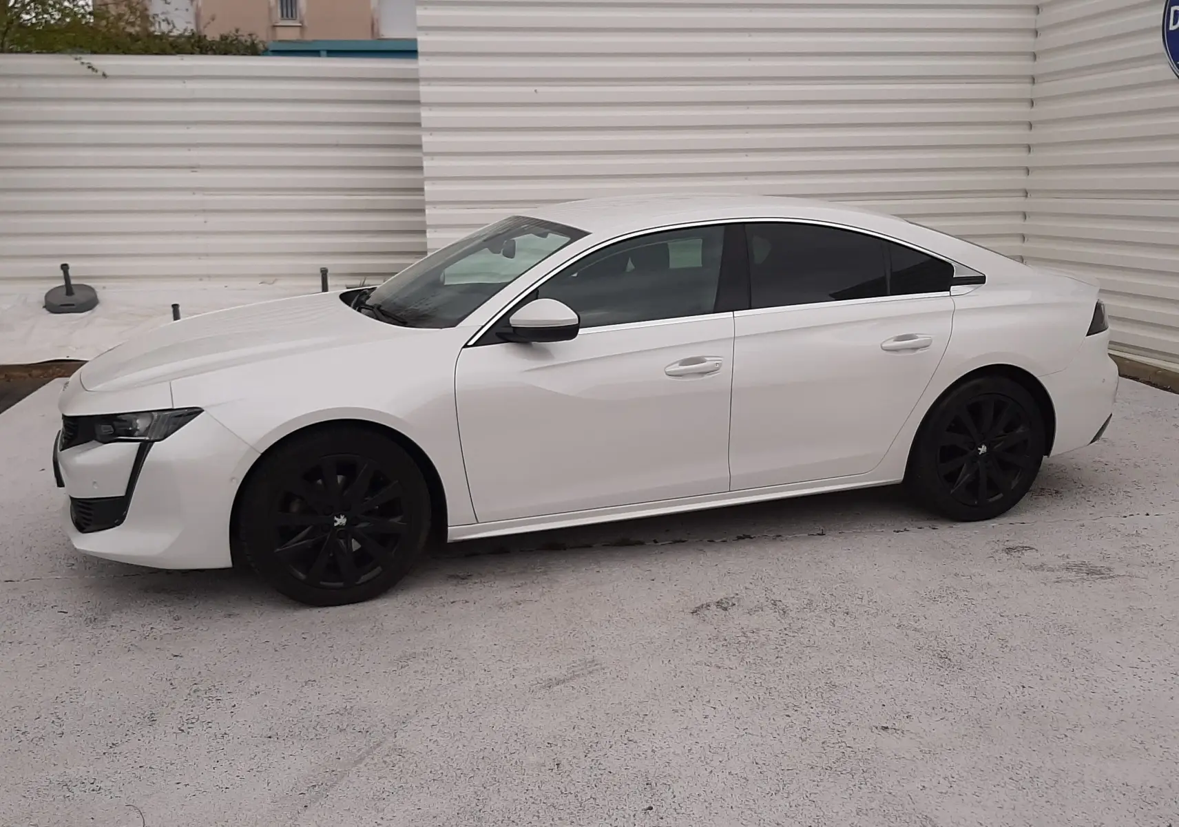 Peugeot 508 blanc vue de profil côté gauche, avec jantes noires et vitres teintées, stationnée sur sol clair.