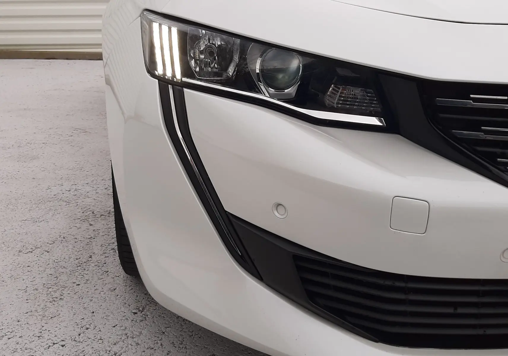 Gros plan sur l'avant gauche blanc d'une Peugeot 508 2019, mettant en valeur son phare LED vertical et la calandre noire.