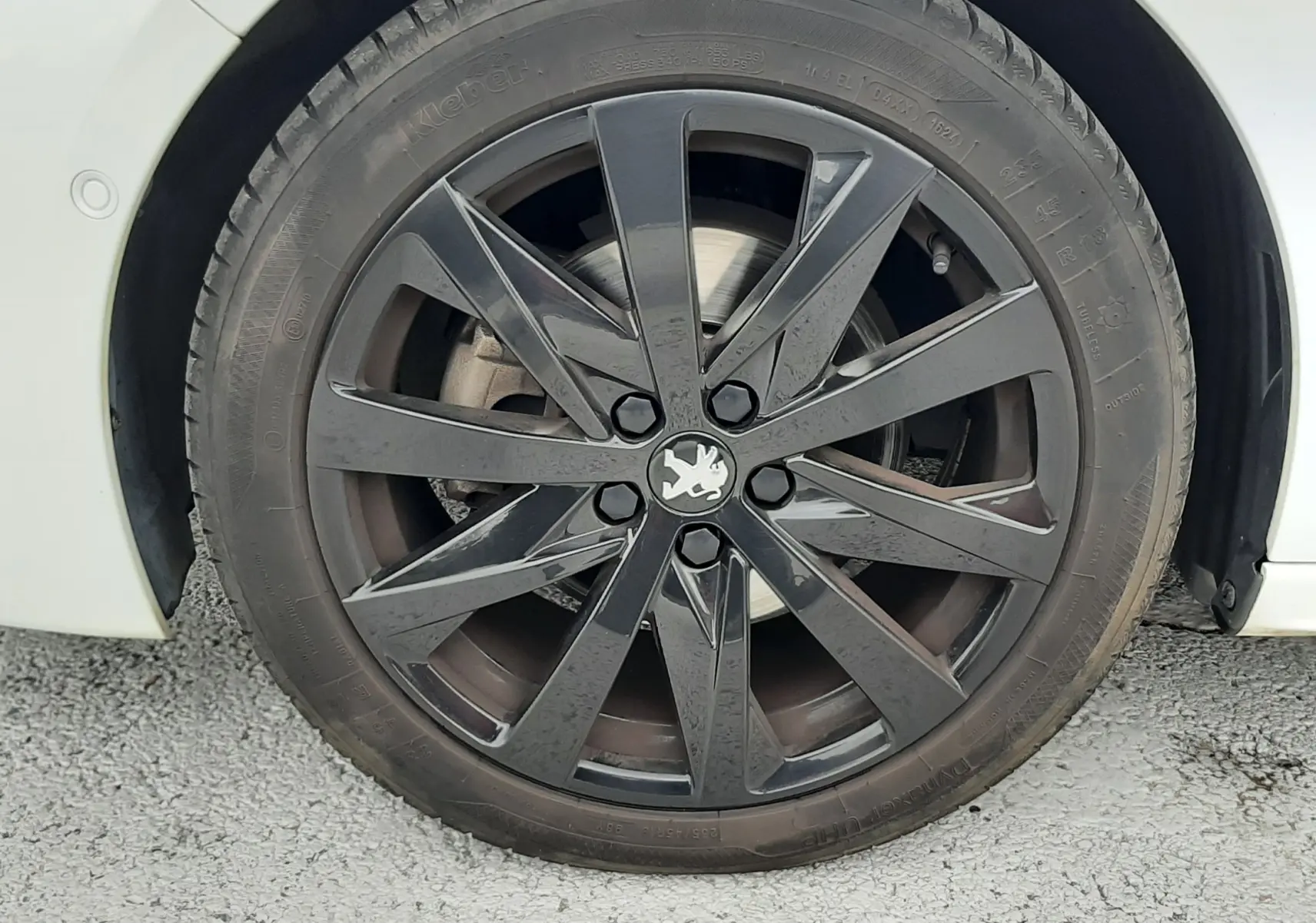 Gros plan sur la roue avant droite d'une Peugeot 508 blanche avec jante alliage noire au design moderne.