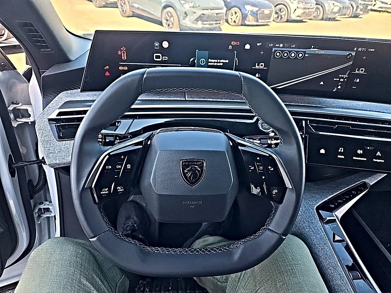 Vue intérieure centrée sur le volant cuir noir et les écrans digitaux du tableau de bord du Peugeot 5008 Hybrid 145 blanc.