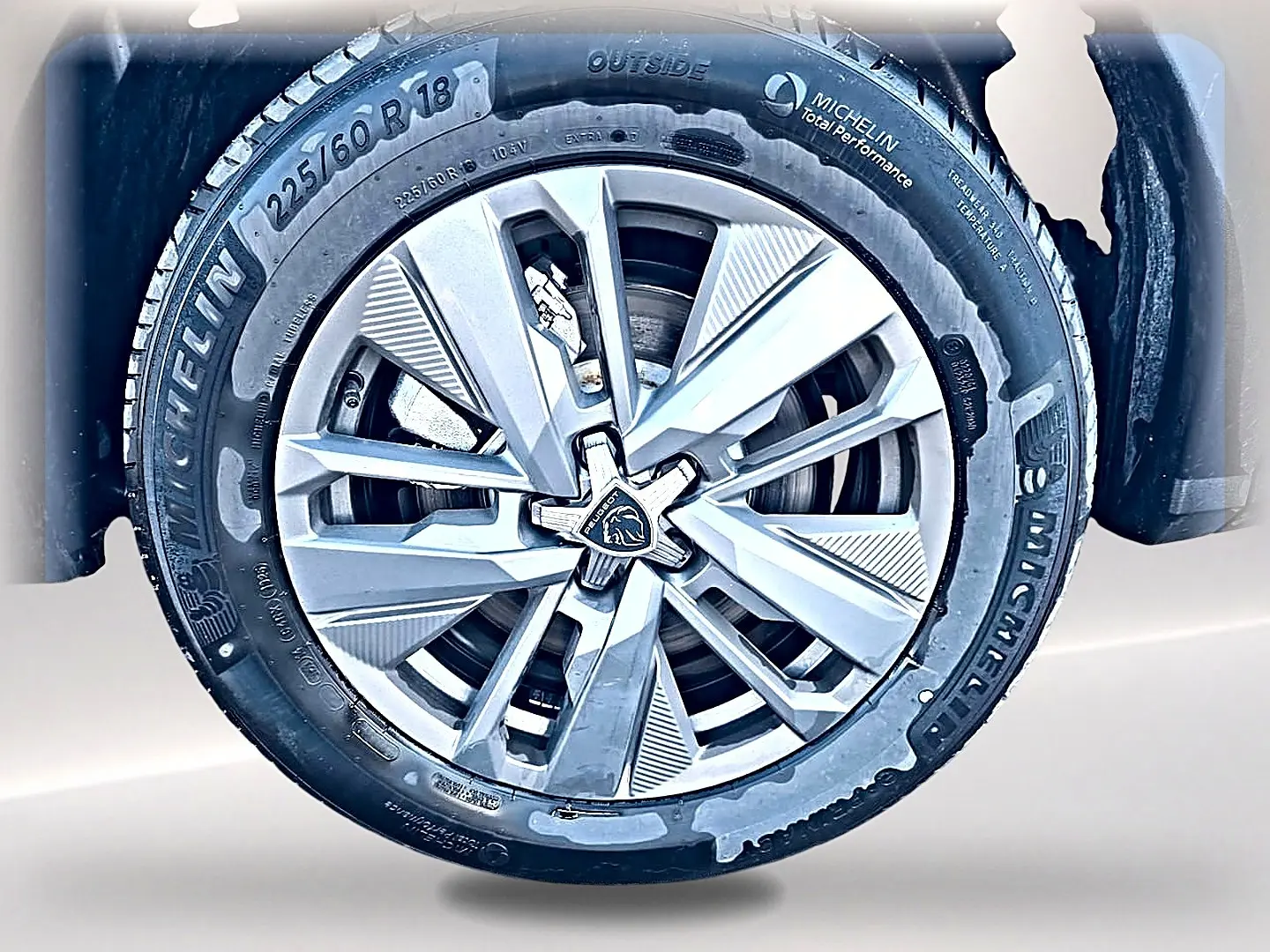 Gros plan sur la jante alu 18 pouces Michelin d’un Peugeot 5008 blanc, mettant en valeur le logo Peugeot central.