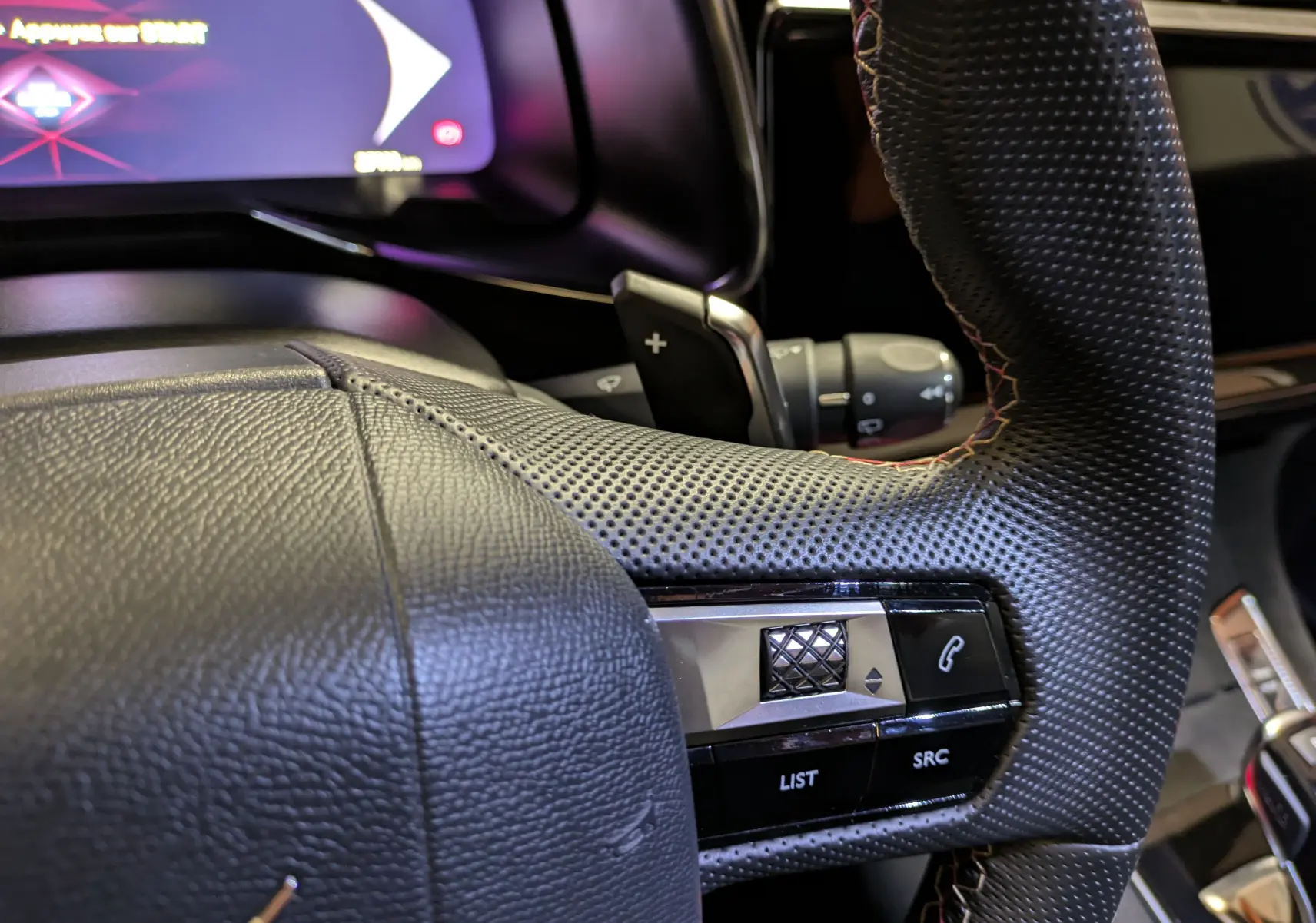 Gros plan sur le volant en cuir perforé noir du DS7 2023 avec commandes intégrées et affichage numérique partiel.