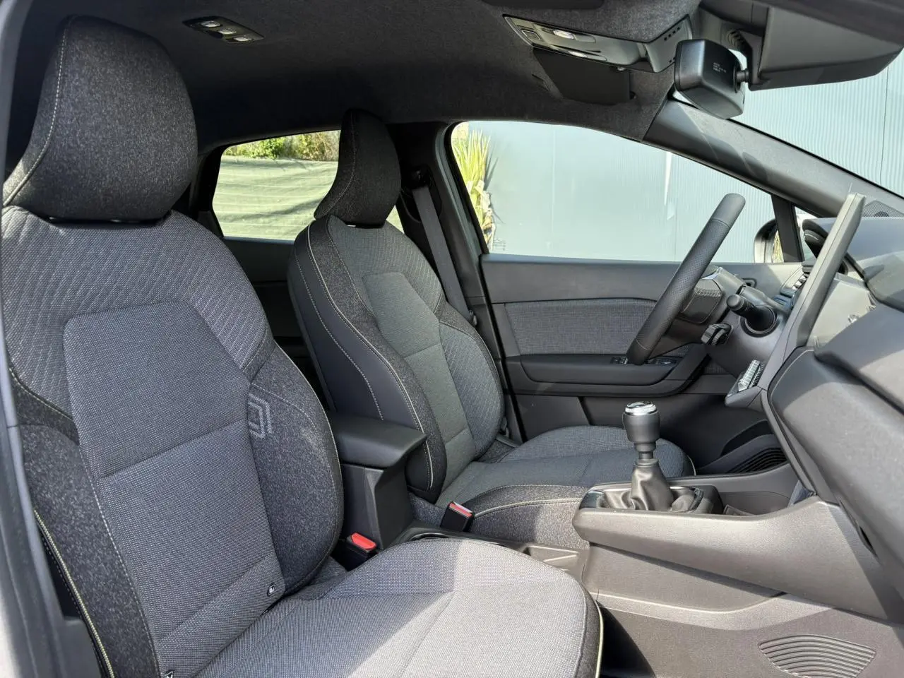 Vue intérieure côté conducteur du Renault Captur 2025, sièges gris et levier de vitesses manuel visible.