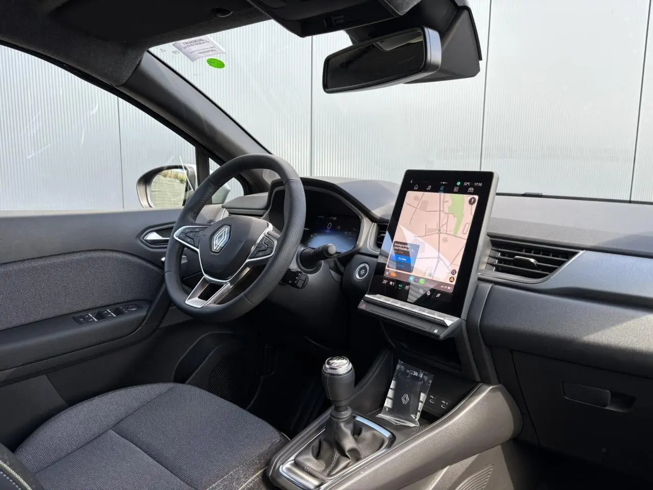 Vue intérieure côté conducteur du Renault Captur 2025 avec tableau de bord noir et écran tactile vertical affichant la navigation.