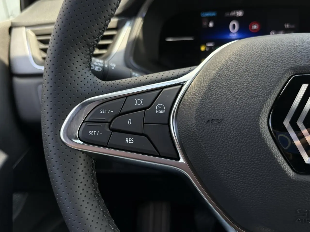 Gros plan sur le volant perforé côté gauche du Renault Captur 2025 avec commandes intégrées et logo central chrome.