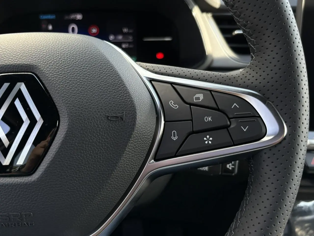 Gros plan sur le volant perforé noir du Renault Captur 2025 avec commandes multifonctions et logo central chromé.