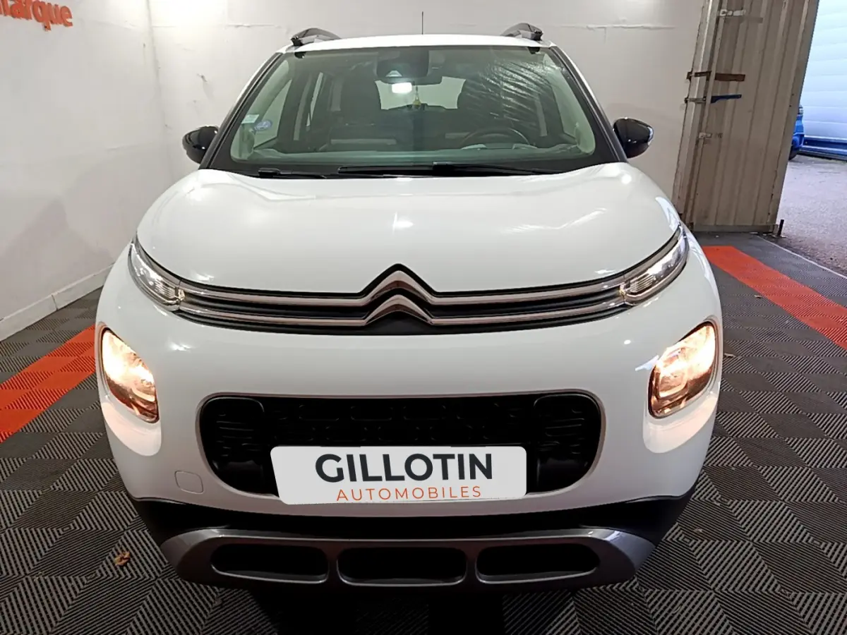 Vue avant d'une Citroën C3 Aircross blanche avec feux allumés et calandre noire dans un garage.