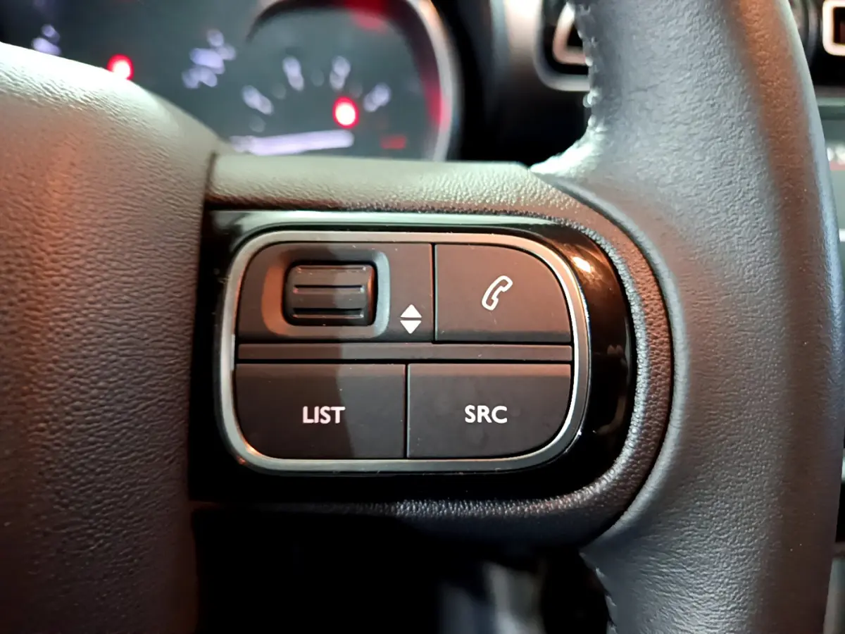 Gros plan sur les commandes gauche du volant cuir noir du Citroën C3 Aircross blanc, avec boutons LIST et SRC visibles.